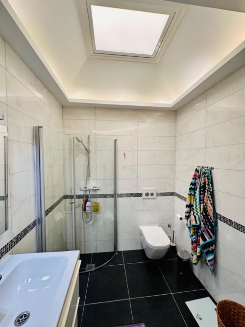 Baño moderno en villa de Nerja con ducha de cristal, inodoro blanco, baldosas negras, claraboya y toallas coloridas