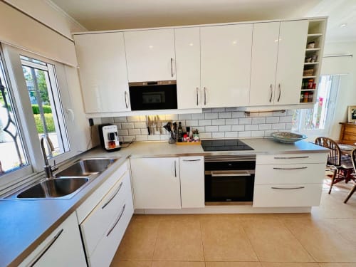 Cocina blanca moderna en villa de Nerja con electrodomésticos de acero inoxidable, azulejos tipo metro y vistas al jardín desde el patio