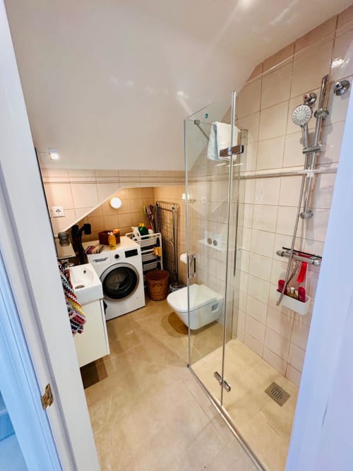 Baño moderno con cabina de ducha de cristal, azulejos blancos y lavadora en villa de Nerja