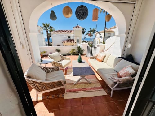 Soleada terraza de villa en Nerja con zona de descanso, vistas al mar, palmeras y linternas decorativas colgantes