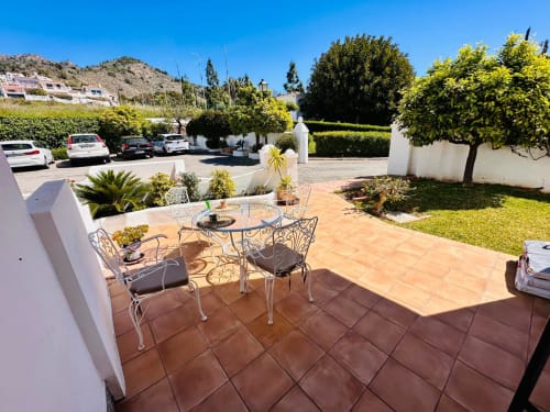 Patio de barro cocido con asientos de hierro forjado en villa Nerja Holiday Homes, con vistas a jardines cuidados y autos estacionados