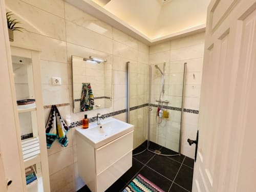 Baño moderno en villa de Nerja con lavabo blanco, ducha con mamparas de cristal, suelo de baldosas negras y detalles decorativos