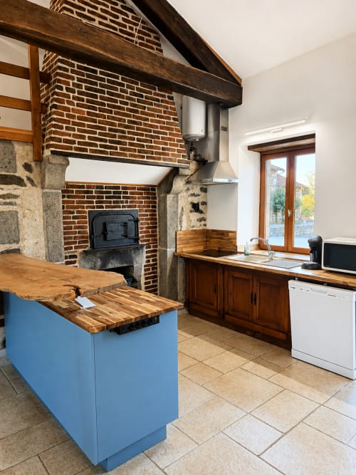 Rustic cottage kitchen at Domaine de Beau Site with blue island, exposed beams, brick fireplace and garden views