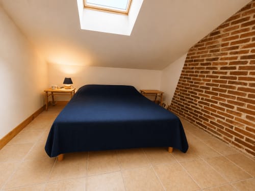 Cozy attic bedroom with dark blue bed, exposed brick wall, skylight, and wooden side tables at Domaine de Beau Site