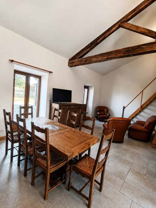 Spacious dining room in La Longère cottage at Domaine de Beau Site with wooden beams, dining table, leather armchairs, and