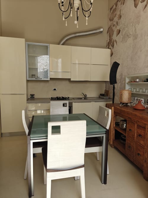 Zona cucina-pranzo moderna nell'appartamento LHE Coco's Home a Cesena con credenza color crema, piano cottura a gas e tavolo da pranzo in vetro