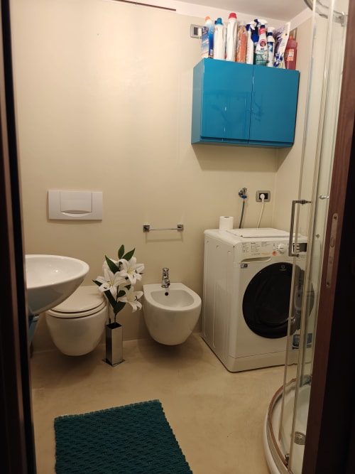 Bagno luminoso con toilette, bidet, lavatrice asciugatrice, mobiletto blu e piastrelle bianche nell'appartamento Coco's Home di LHE