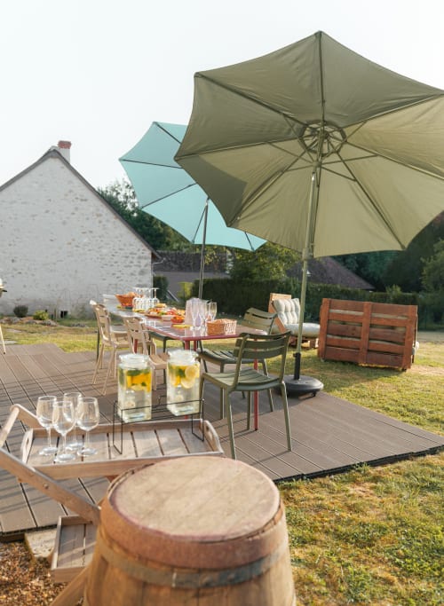 Coin repas en plein air au Hameau de Céline avec parasols, table dressée et chaumière dans les Landes, France