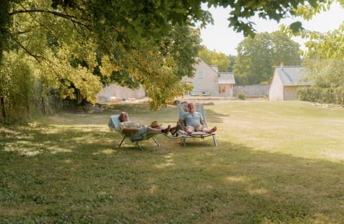 Deux clients détendus dans des chaises sous les arbres du jardin pastoral du Hameau de Céline, une maison d'hôtes française