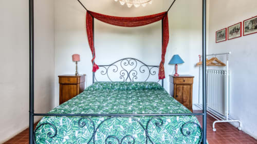 Camera elegante del Borgo Rinascimento B&B a Farnese con letto in ferro battuto ornato, biancheria verde floreale, drappeggi rossi a baldacchino e