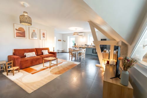 Espace de vie ouvert et moderne au gîte Le Hameau de Céline en Landes-le-Gaulois avec canapé orange, poutres en bois naturel