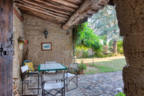 Terrazza coperta a Borgo Rinascimento con muri in pietra, travi in legno, tavolo da gioco e cortile ricoperto d'edera a Farnese