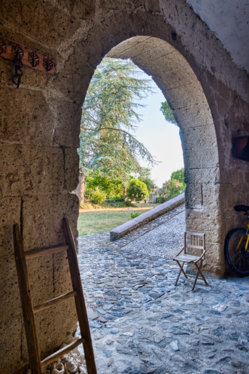Ingresso in pietra con arco a Borgo Rinascimento, Farnese: cortile in ciottoli e vista sulla campagna