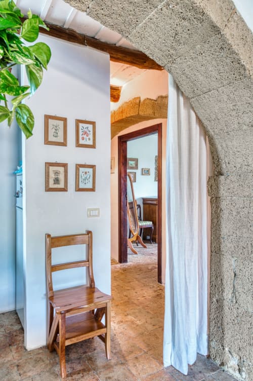 Ingresso dell'appartamento Giotto a Borgo Rinascimento, Farnese, con sedia in legno e opere botaniche su muri imbiancati