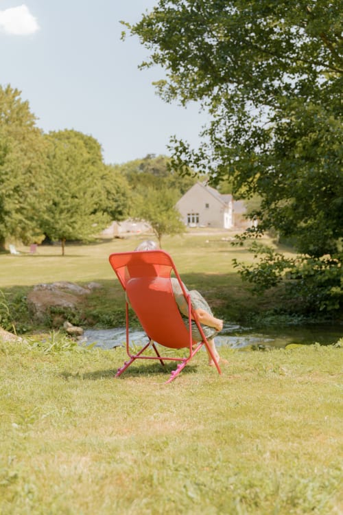 Hôte relaxant dans un fauteuil rouge au bord du ruisseau au Hameau de Céline, gîte en Landes-le-Gaulois, France