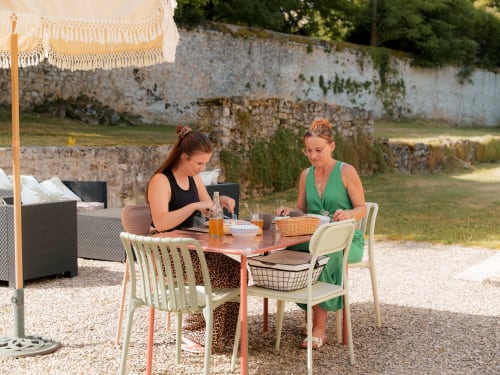 Deux femmes dînant en terrasse au gîte Le Hameau de Céline en Landes, France, avec murs de pierre rustiques en arrière-plan