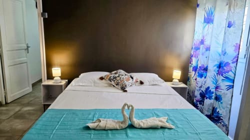 Chambre double aux Deux Cocotiers avec cygnes en serviettes, chemin de lit turquoise et rideaux fleuris à Sainte-Luce