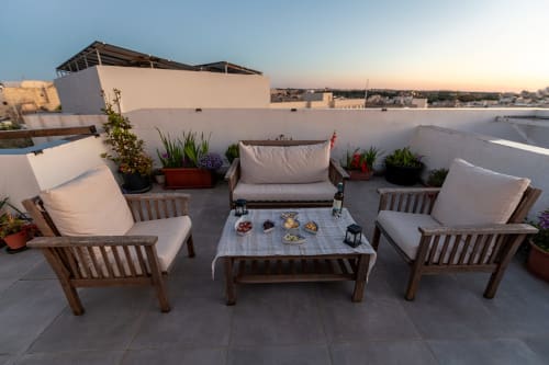 Rooftop terrace at Estrella Lodging in Rabat with wooden seating, cushions, potted plants, and city views at sunset.