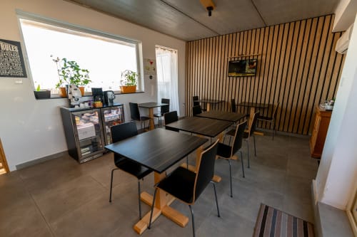 Modern hotel common area at Estrella Lodging in Rabat with dining tables, chairs, refrigerator, and vertical wood-slat wall
