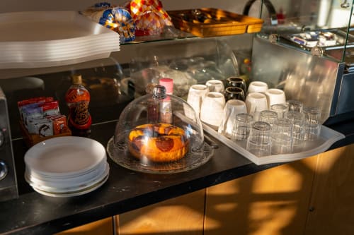 Hotel room buffet counter at Estrella Lodging with pastry under dome, white plates, glasses, and red sauce bottles