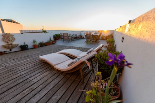 Sunset terrace at Estrella Lodging in Rabat with wooden lounge chair, purple flowers, and city views