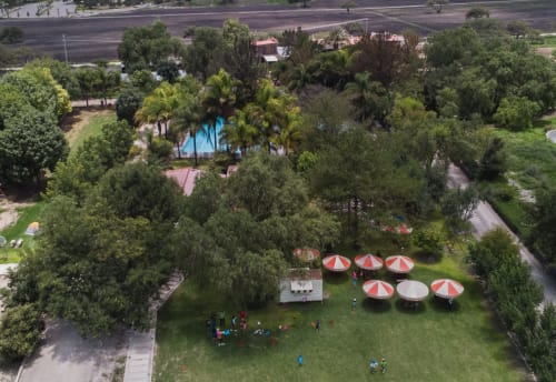 Jardín del Hotel El Porvenir con sombrillas rojo y blanco, césped verde exuberante y árboles altos en Querétaro, México
