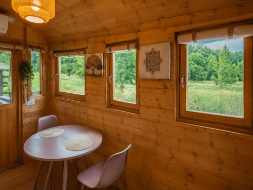 Intérieur douillet de chalet en bois avec table ronde, chaises, grandes fenêtres donnant sur la forêt des Cévennes et les montagnes