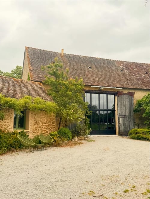Entrée du gîte Maisons Noisette à Saint-Pierre-des-Ormes : façade en pierre, murs couverts de lierre et portes modernes noires
