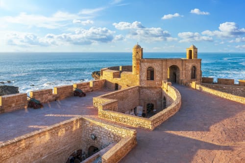 Ancienne forteresse en pierre dominant la mer Méditerranée turquoise sous un ciel bleu nuageux