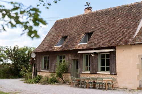 Maisons Noisette B&B à Saint-Pierre-des-Ormes : chaumière rustique en pierre avec colombages, toit d'ardoise, espace repas extérieur.