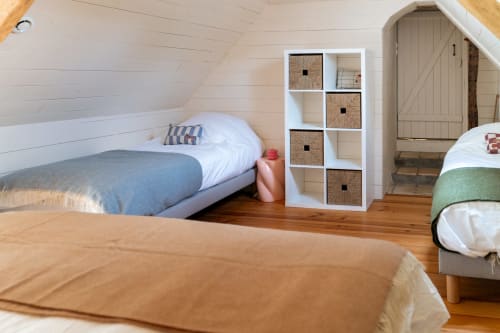 Chambre sous les combles douillette aux Maisons Noisette B&B avec lits jumeaux, murs blancs à clins et rangements en osier.