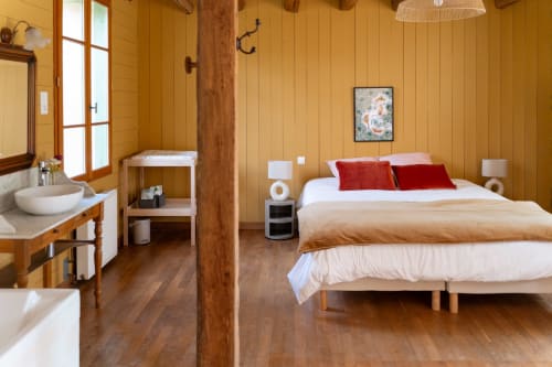 Chambre chaleureuse aux Maisons Noisette avec lit queen-size, oreillers rouges, salle de bains privée et charme rustique
