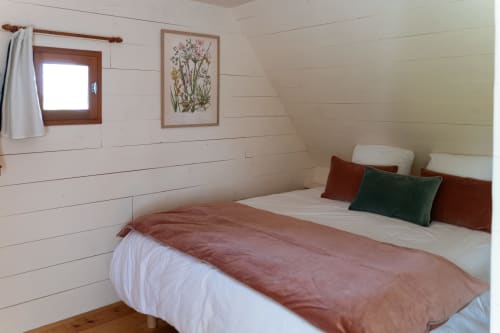Chambre cosy des Maisons Noisette avec murs en lambris blanc, fenêtre encadrée bois et art botanique