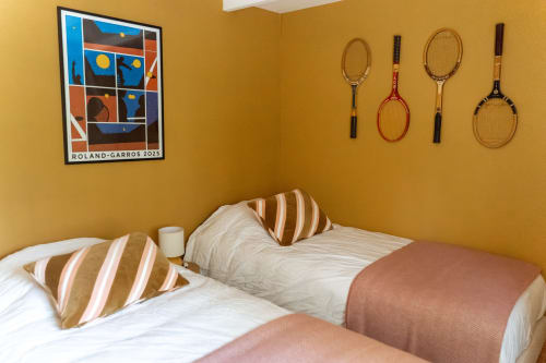 Chambre douillette aux murs jaunes à Maisons Noisette B&B, raquettes de tennis, affiche Roland Garros et oreillers rayés.