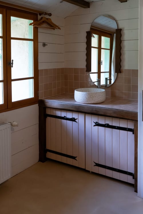 Salle de bains rustique aux Maisons Noisette B&B avec lavabo en pierre, miroir ovale, vanité en bois et portes-fenêtres