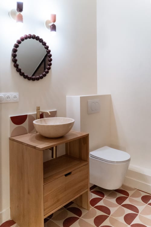Salle de bains moderne à Maisons Noisette avec miroir orné de perles, vanité en bois, lavabo en pierre et carrelage à motifs.