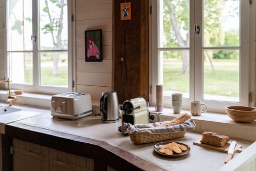 Cuisine lumineuse de la Maison Noisette avec électroménagers, pâtisseries fraîches et vue sur le jardin par les grandes fenêtres