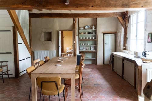 Cuisine-salle à manger rustique aux Maisons Noisette avec poutres en bois, carrelage en terre cuite, table et étagères en bois.
