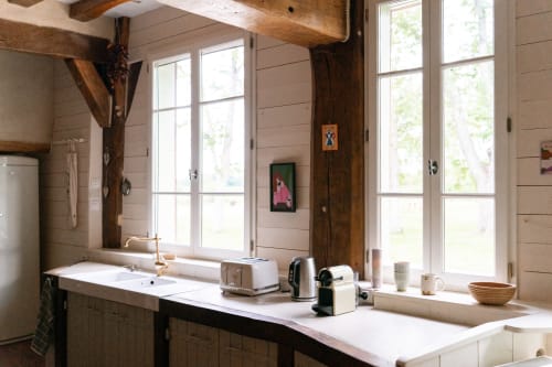 Cuisine rustique à Maisons Noisette avec poutres apparentes, plan de travail blanc et grandes fenêtres sur Saint-Pierre-des-Ormes