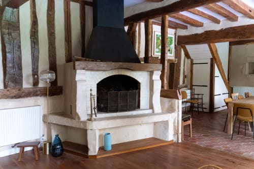 Foyer rustique avec pourtour en pierre blanche et cheminée noire dans une chambre aux poutres apparentes à Maisons Noisette B&B,