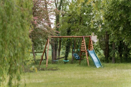 Terrain de jeu rustique avec balançoires et toboggan dans un jardin arborisé à Maisons Noisette, Saint-Pierre-des-Ormes