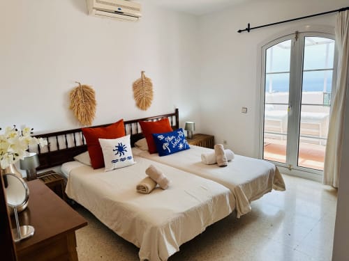Dormitorio luminoso con dos camas, balcón con vistas al mar, arte decorativo en paredes y comodidades modernas en apartamento Nerja Holiday Homes
