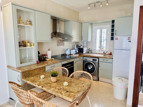 Cocina y comedor modernos en apartamento de Nerja Holiday Homes con encimeras de granito, armarios blancos y sillas de mimbre