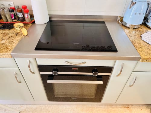 Cocina moderna con placa de inducción negra, horno integrado, encimeras de granito y electrodomésticos de acero inoxidable en Nerja
