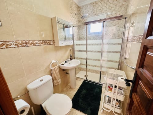 Baño moderno en apartamento de Nerja con ducha, lavabo de pedestal, inodoro y piso oscuro