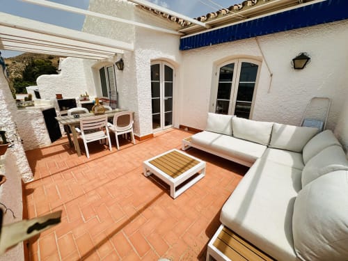 Terraza de terracota luminosa en Nerja Holiday Homes con mobiliario blanco, comedor y vistas al mar en este exclusivo apartamento
