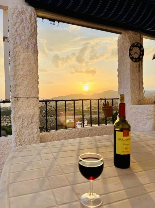 Vista del atardecer desde el balcón del exclusivo apartamento de Nerja con copa de vino y botella Bardesa frente al paisaje mediterráneo
