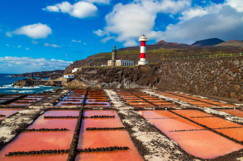 Estanques de sal coloridos y faro en la costa rocosa de La Palma bajo cielo azul