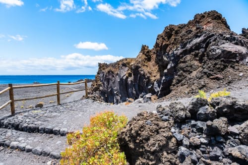 Rocas de lava negra volcánica y paisaje costero en La Palma con océano azul y cerca de madera