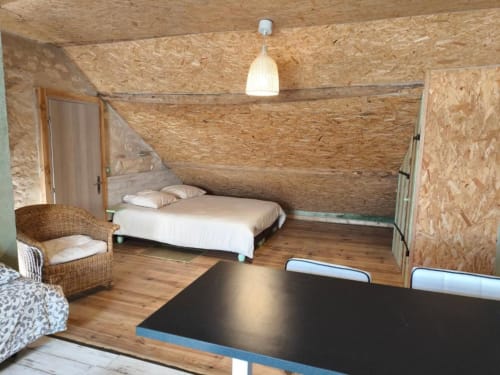 Chambre rustique à la Madiana 89 B&B à Bellechaume avec murs en liège, lit en bois, fauteuil en osier et équipements modernes